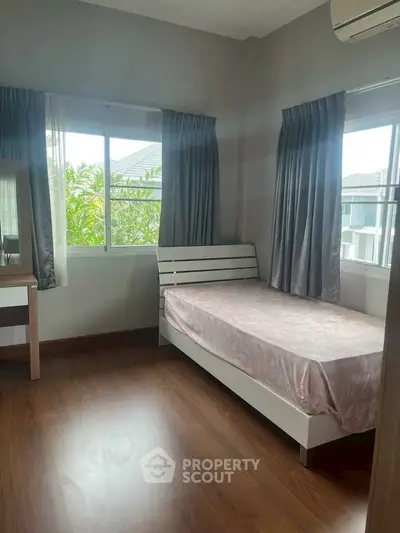 Cozy bedroom with single bed and natural light from large windows.