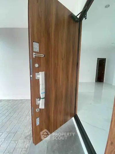 Modern wooden door opening to a spacious and bright interior with sleek flooring.