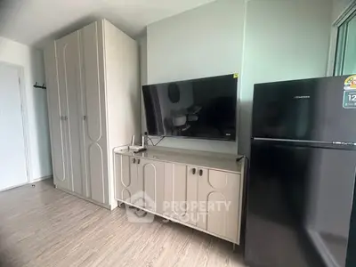 Modern living room with sleek cabinetry and flat-screen TV, featuring a stylish refrigerator.