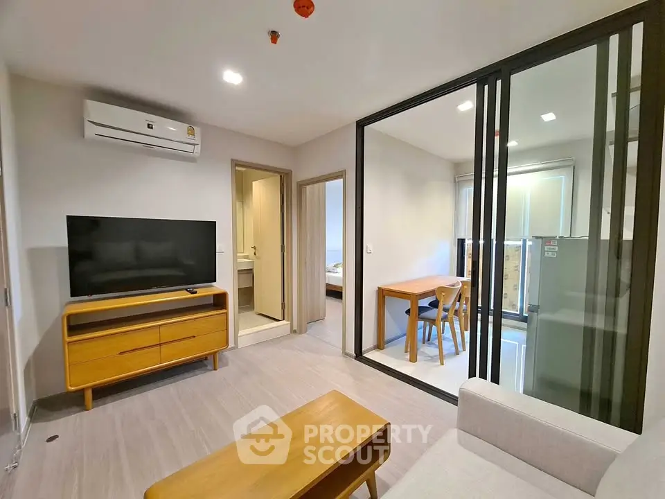 Modern living room with sleek furniture and glass partition leading to dining area.