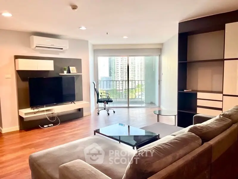 Spacious modern living room with large balcony and city view, featuring sleek furniture and wooden flooring.