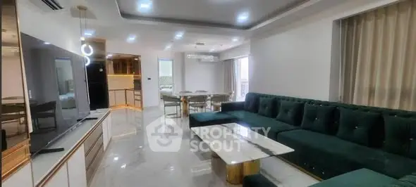 Luxurious modern living room with elegant green sofa and marble coffee table, open to dining area and kitchen.