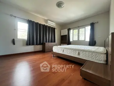 Spacious bedroom with wooden flooring and large windows for natural light.