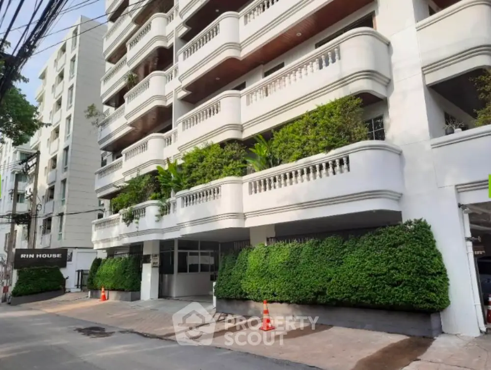 Elegant multi-story building with lush greenery and spacious balconies in urban setting