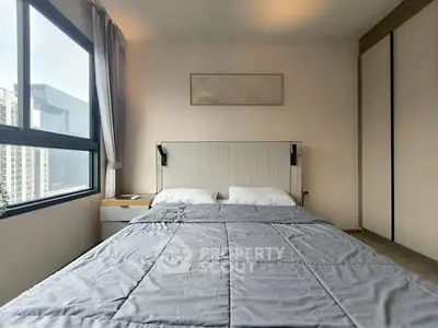 Modern bedroom with large window and stylish decor in urban apartment.