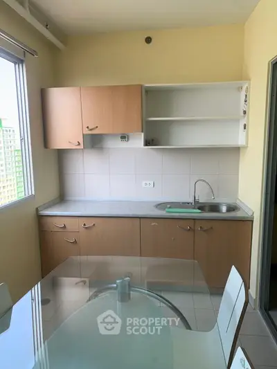 Compact kitchen with wooden cabinets and glass dining table, featuring a bright window view.