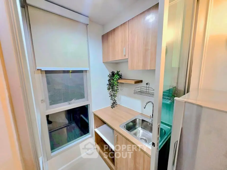 Modern compact kitchen with wooden cabinets and large window, perfect for urban living.