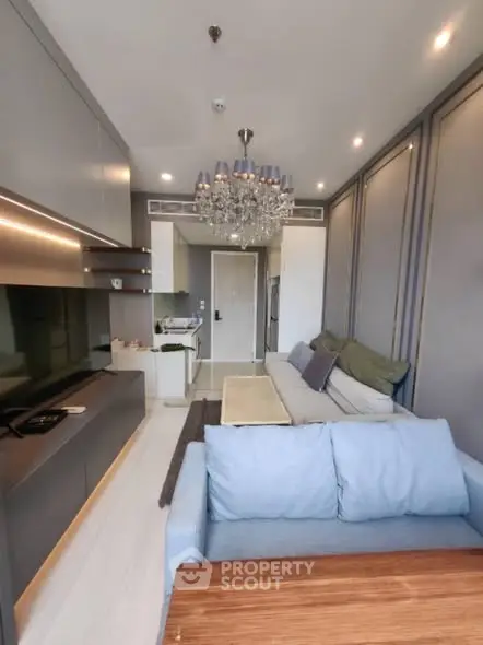 Modern living room with elegant chandelier and open kitchen layout in a stylish apartment.