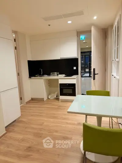 Modern kitchen with sleek design and open layout, featuring a glass dining table and stylish green chairs.
