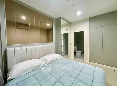 Modern bedroom with mirrored wardrobe and ensuite bathroom in stylish apartment.