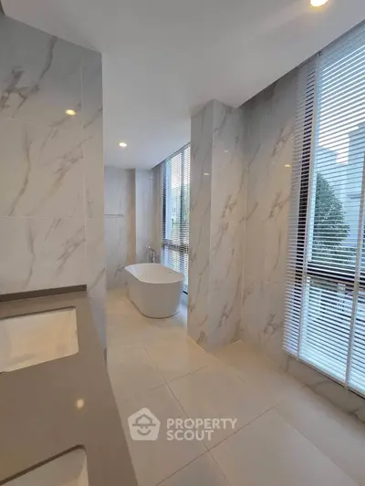Luxurious bathroom with marble tiles and freestanding bathtub, featuring large windows for natural light.