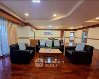 Spacious living room with elegant wooden flooring and modern black leather sofas.