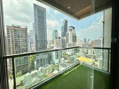 Stunning cityscape view from a modern high-rise balcony with glass railing and artificial grass flooring.