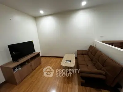 Cozy living room with wooden flooring, brown sofa, and flat-screen TV on a wooden stand.