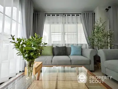 Elegant living room with stylish gray sofa and vibrant cushions, featuring large windows and lush indoor plants.