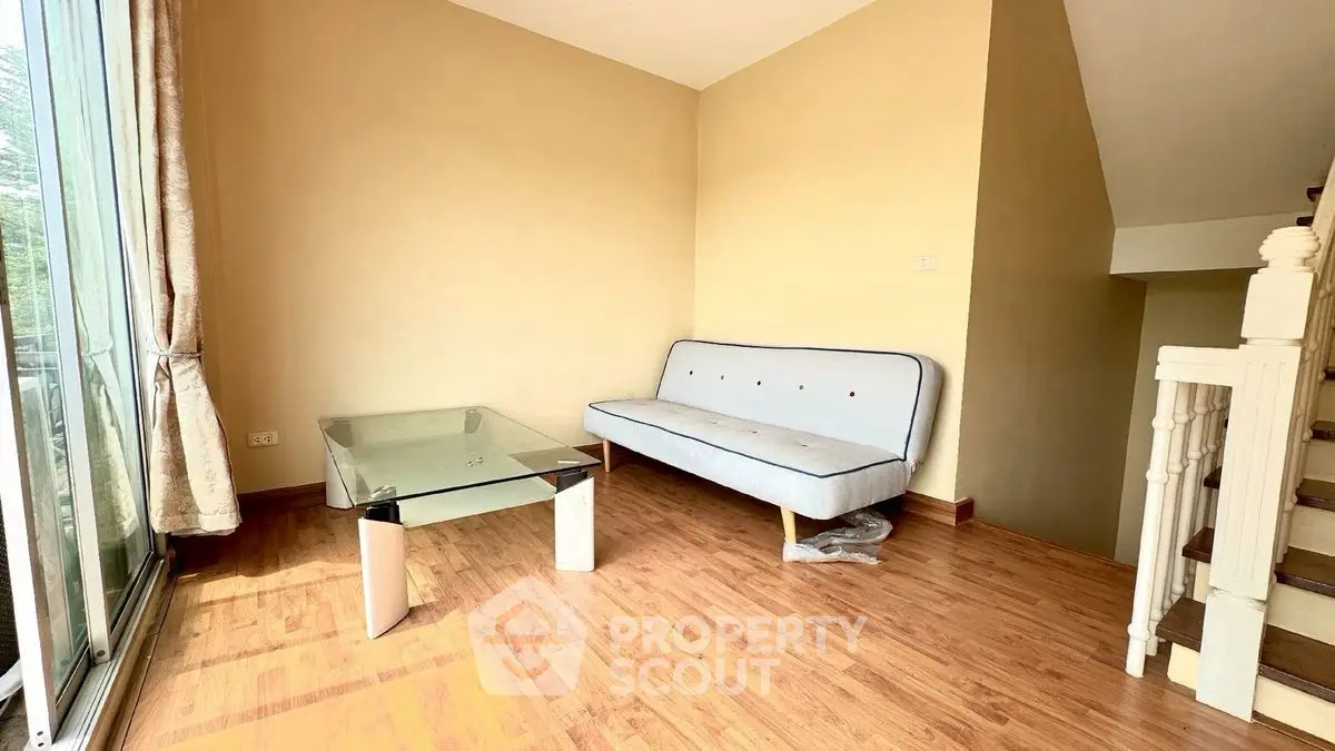 Cozy living room with glass coffee table and sofa, featuring wooden flooring and natural light.