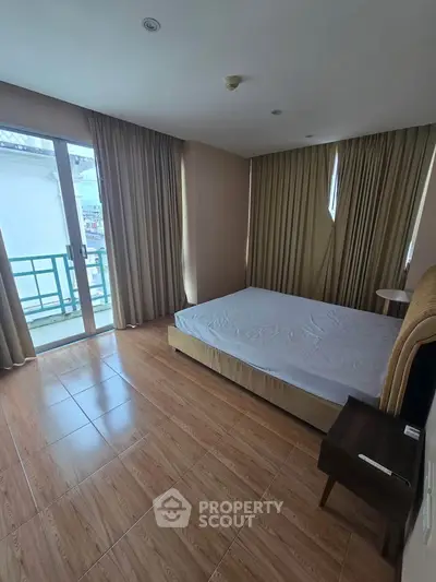 Spacious bedroom with large windows and balcony access, featuring elegant curtains and wooden flooring.