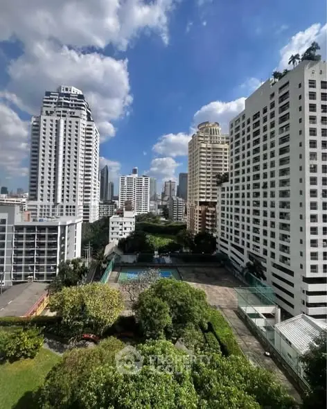 Stunning cityscape view from high-rise building with lush greenery and pool area.