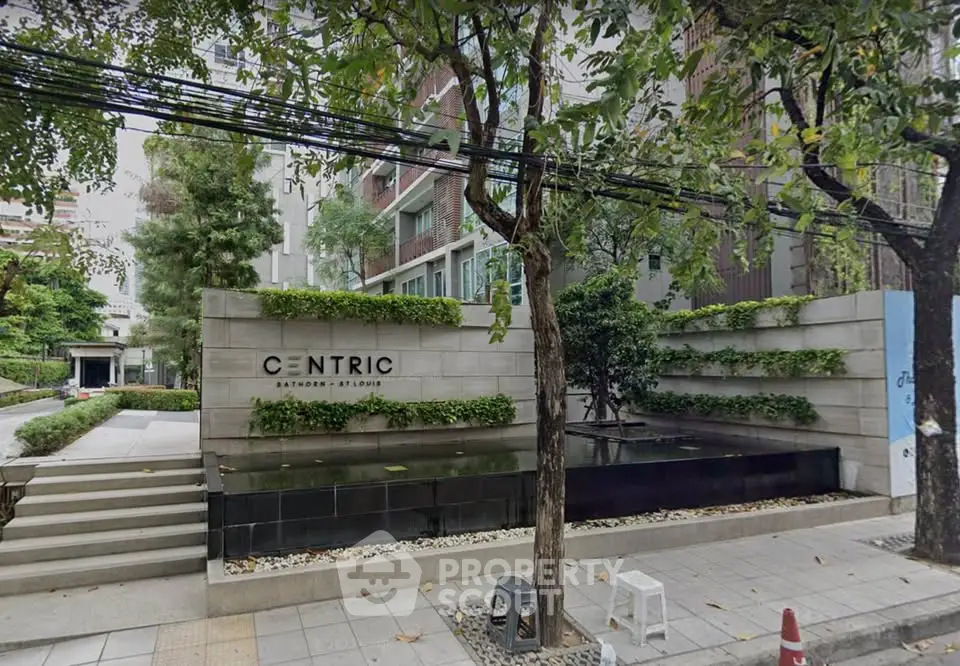 Modern condominium entrance with lush greenery and sleek design in urban setting.