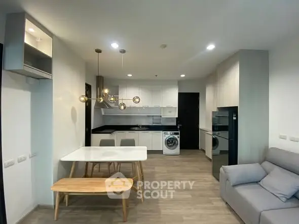 Modern open-layout living room with kitchen and dining area, featuring stylish lighting and contemporary furniture.