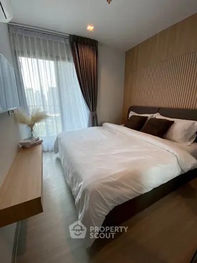 Modern bedroom with cozy bedding and city view through large window.