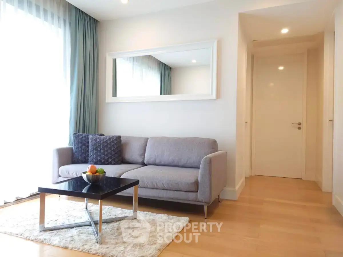 Modern living room with stylish sofa, large mirror, and natural light from floor-to-ceiling window.
