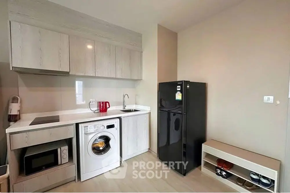 Modern compact kitchen with washing machine and fridge in sleek apartment.