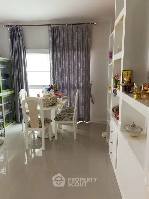 Elegant dining area with white furniture and decorative shelves in a cozy home setting.