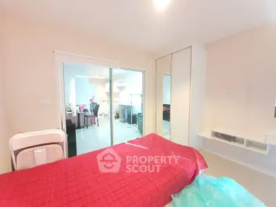 Spacious bedroom with modern furnishings and sliding glass doors leading to a bright kitchen area.
