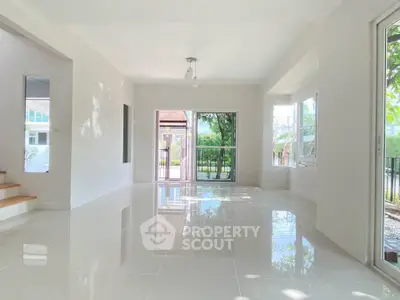 Spacious and bright living room with large windows and glossy tiled floors, offering a serene garden view.