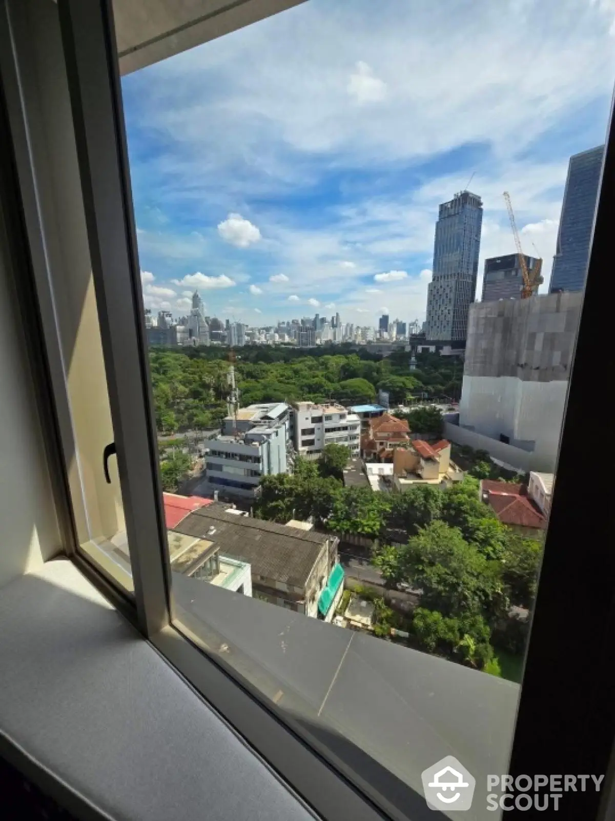 Stunning cityscape view from high-rise window overlooking lush greenery and skyline.