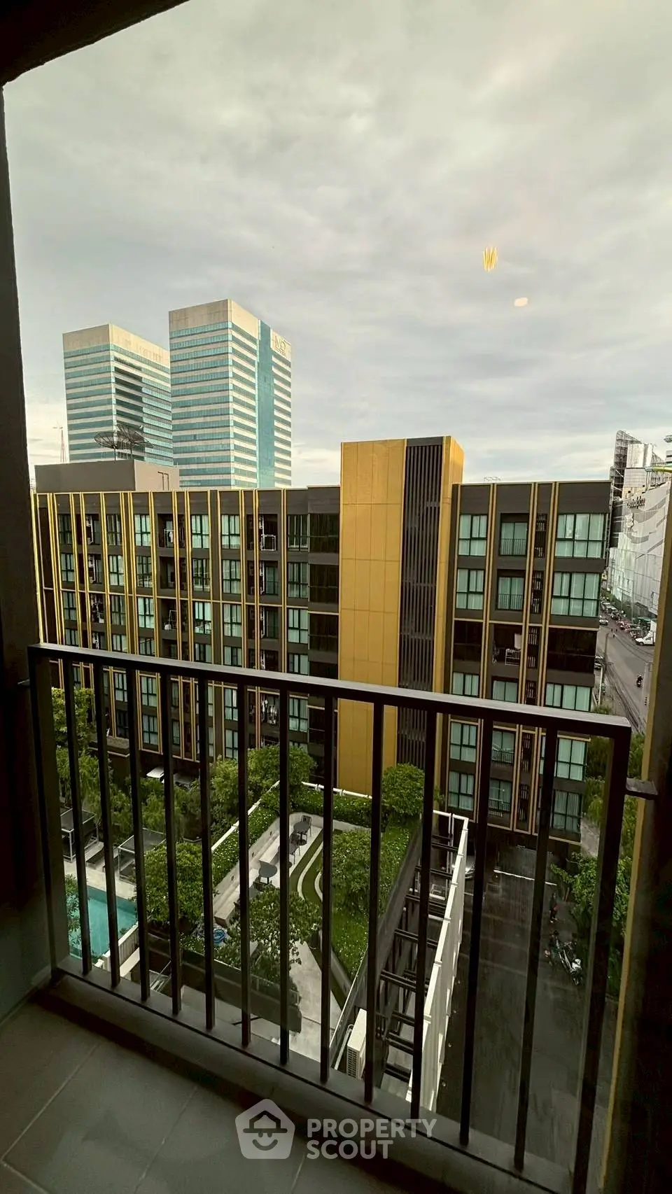 Stunning cityscape view from a modern apartment balcony overlooking urban architecture and lush greenery.
