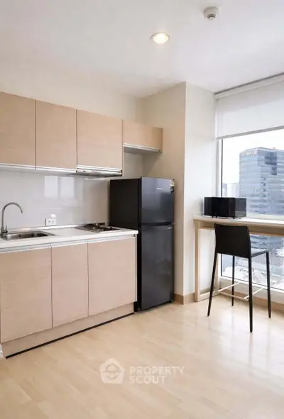 Modern kitchen with sleek cabinets and city view, featuring compact fridge and breakfast bar.