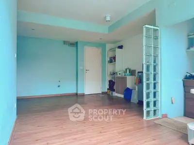 Spacious empty room with wooden flooring and glass block partition in modern apartment.