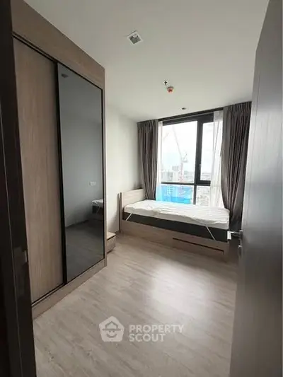 Modern bedroom with large window and wooden flooring, featuring a sleek wardrobe and cozy bed.