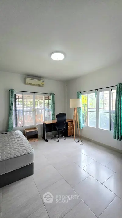Spacious bedroom with natural light, featuring a bed, desk, and large windows with green curtains.
