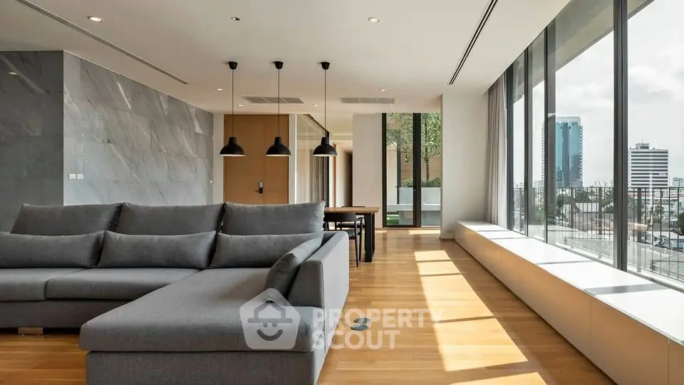 Spacious modern living room with large windows and city view, featuring sleek furniture and elegant lighting.