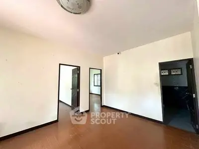 Spacious empty room with wooden flooring and multiple doorways