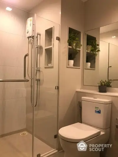 Modern bathroom with sleek glass shower enclosure, white ceramic fixtures, and refreshing greenery adding a touch of nature.