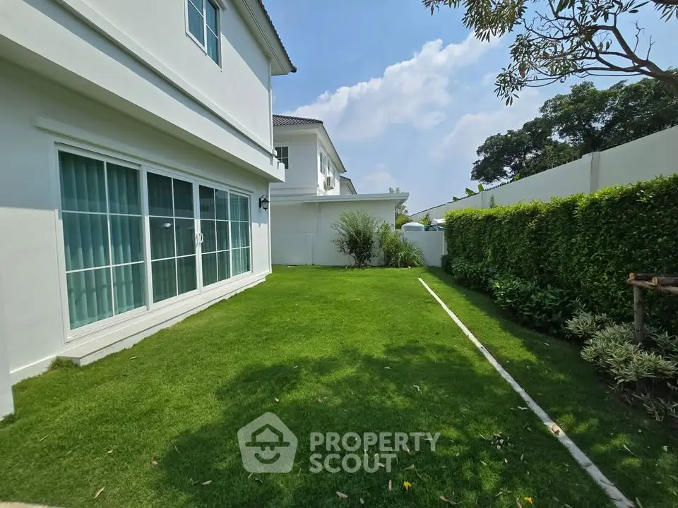 Spacious green garden area with modern white house exterior and lush landscaping.