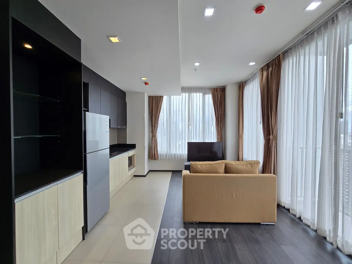 Spacious modern living room with open kitchen and large windows offering ample natural light.