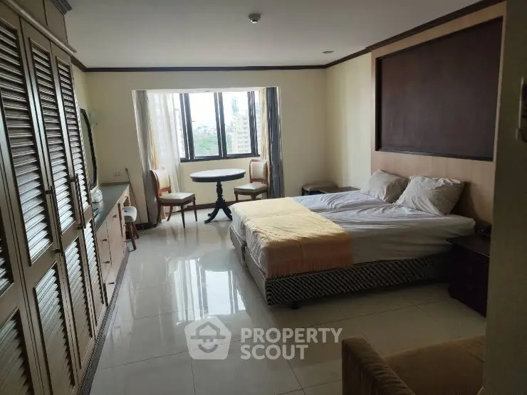 Spacious bedroom with large windows and city view, featuring cozy bed and seating area.