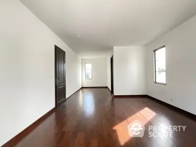 Spacious and sunlit empty room with polished hardwood floors, pristine white walls, and multiple windows inviting natural light, perfect for a personalized living space.