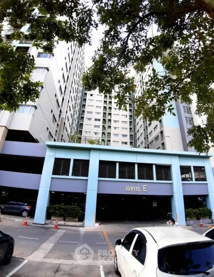 Modern high-rise building exterior with parking area and lush greenery.