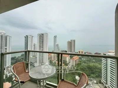 Stunning high-rise balcony with panoramic city and ocean views, featuring cozy outdoor seating.