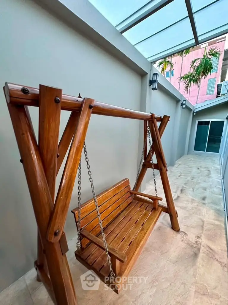 Charming wooden swing in a modern outdoor patio with glass roof.