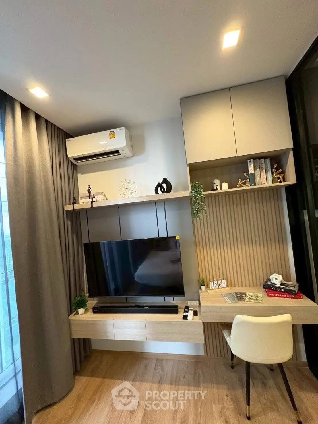 Modern living room with stylish TV setup and cozy workspace, featuring sleek wooden flooring and elegant decor.