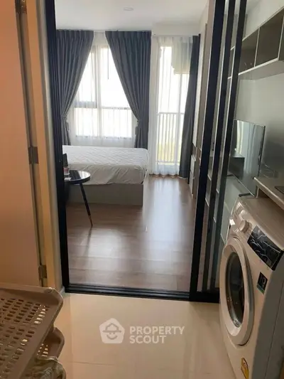 Modern apartment with bedroom and in-unit washing machine, featuring large windows and sleek design.