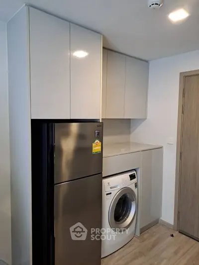 Modern kitchen with sleek cabinets, stainless steel fridge, and built-in washing machine.