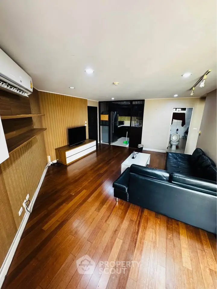 Spacious living room with wooden flooring and modern black leather sofa in a stylish apartment.
